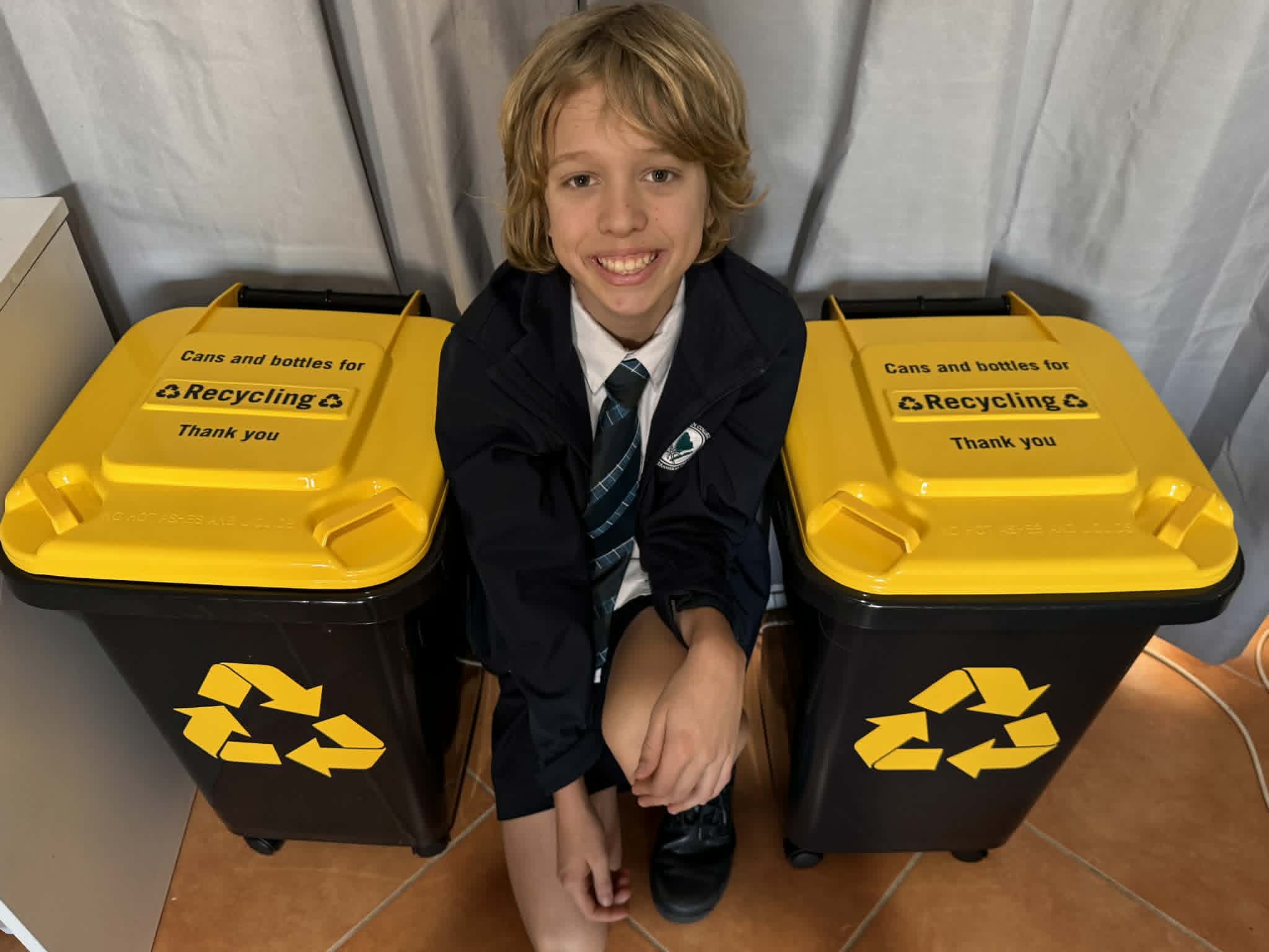Child smiling next to recycling bins